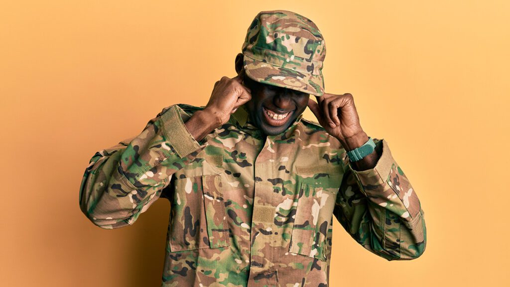 Soldier in camo with fingers over ears to represent hearing loss due to military service